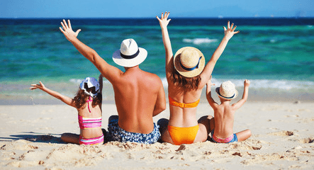 family of 4 sitting on the beach with arms up