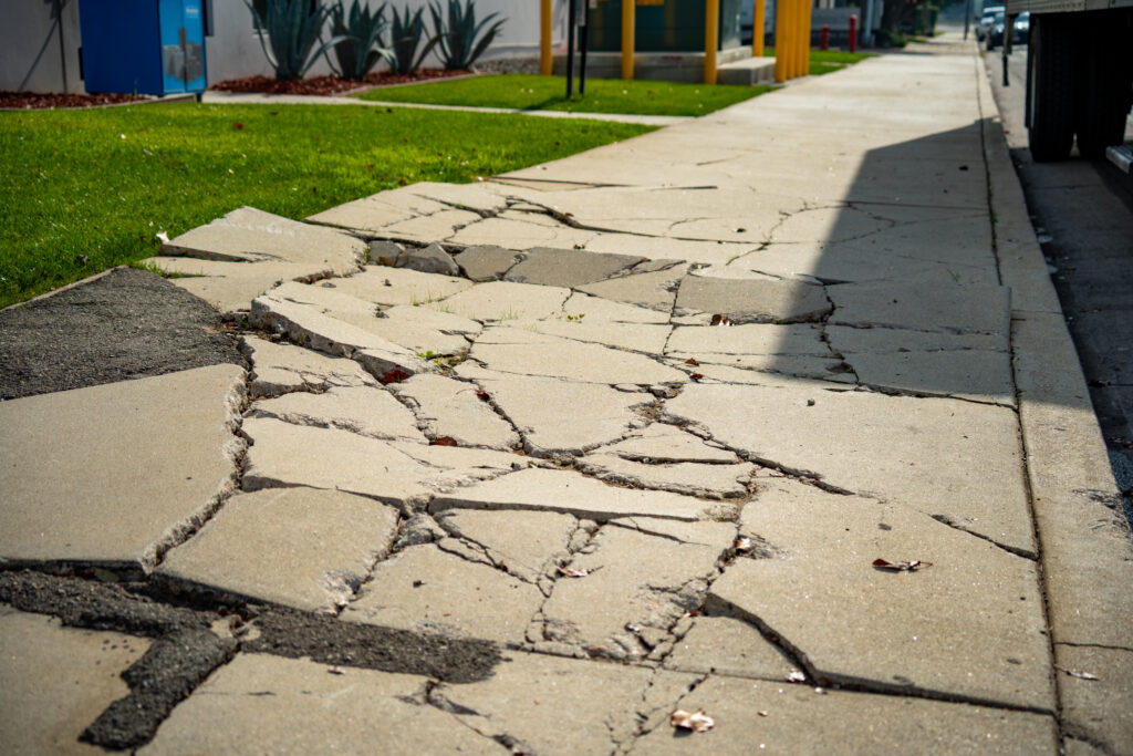 Severely cracked and uneven concrete sidewalk representing a dangerous hazard on a Long Island property where an owner may be liable for an injury.