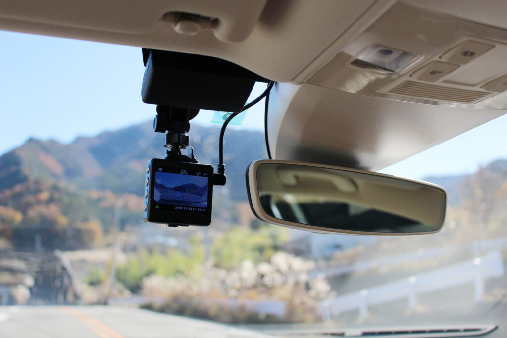A modern dashboard camera mounted on a car windshield next to the rearview mirror, recording the open road ahead to serve as event data recorder evidence in an injury claim.